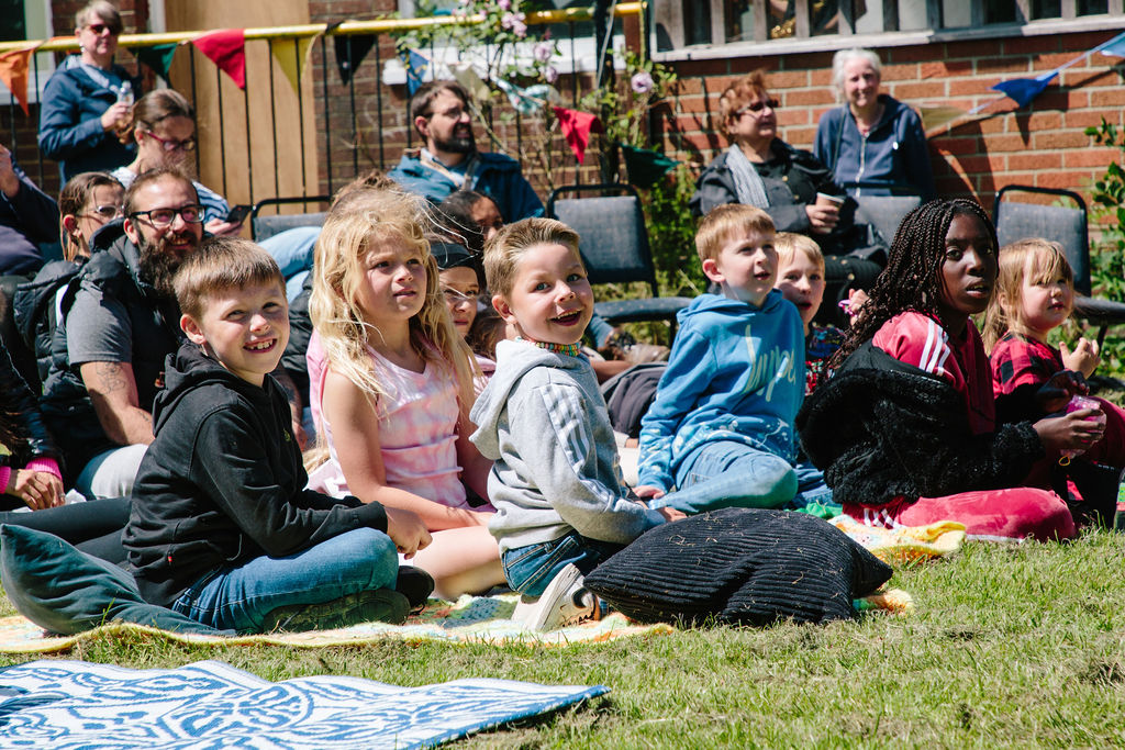 Young children's sitting in the sunshine on the grass enjoying a performance