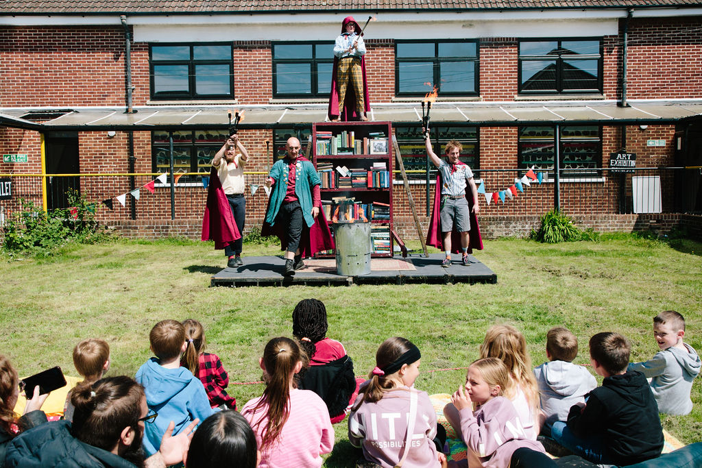 Books performance shot including 4 performers in front of a bookcase. Each performer is holding a flaming torch.